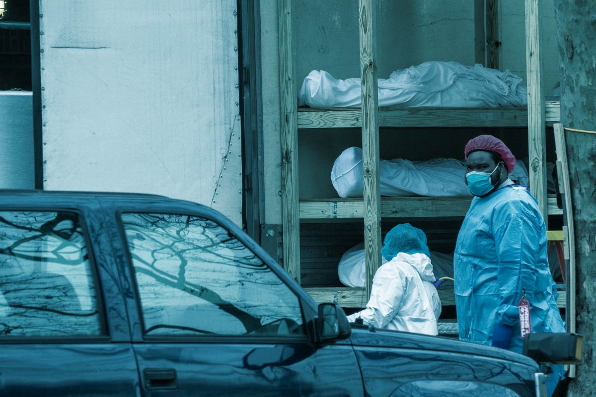 Krankenhausmitarbeiter läuft mit Maske vor aufgebarrten Leichen entlang