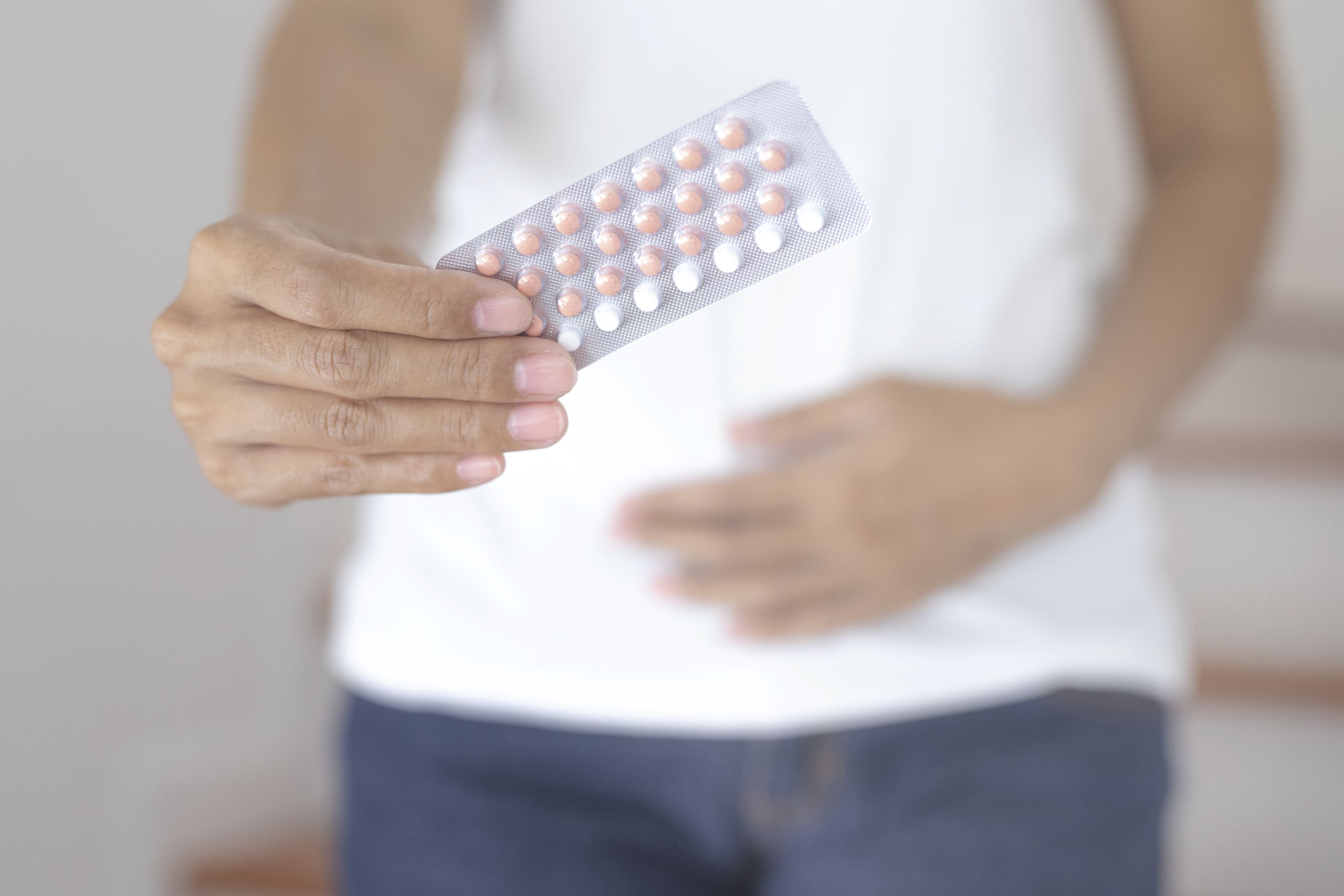 Frau hält Pillenpackung in der Hand und hält sich den Bauch